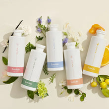 Load image into Gallery viewer, Five Lavido body wash bottles in different scents laid flat with flowers and citrus
